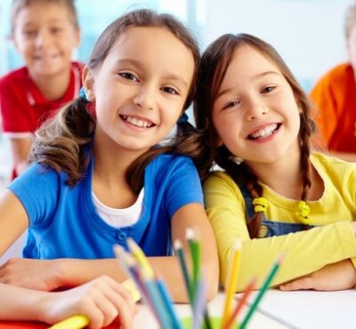 Portrait of two diligent girls looking at camera at workplace with schoolboys on background
